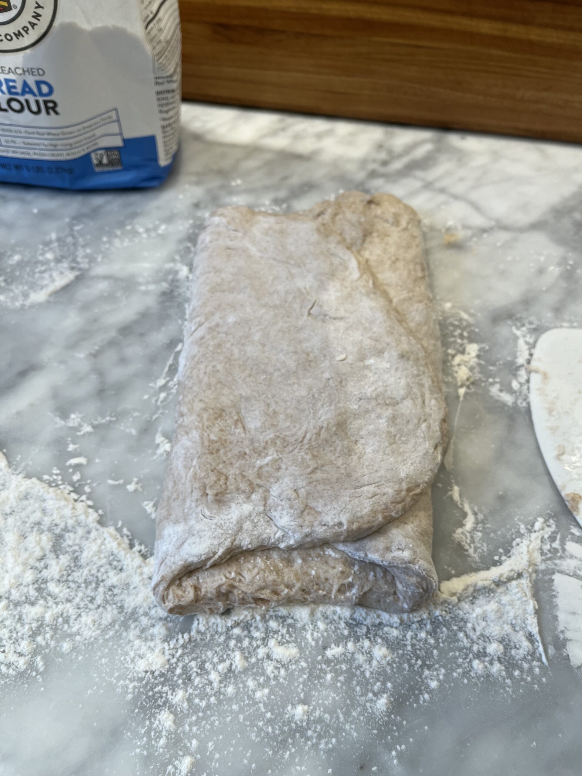 Photo of sourdough bread dough, folded in thirds on a marble counter with flour.