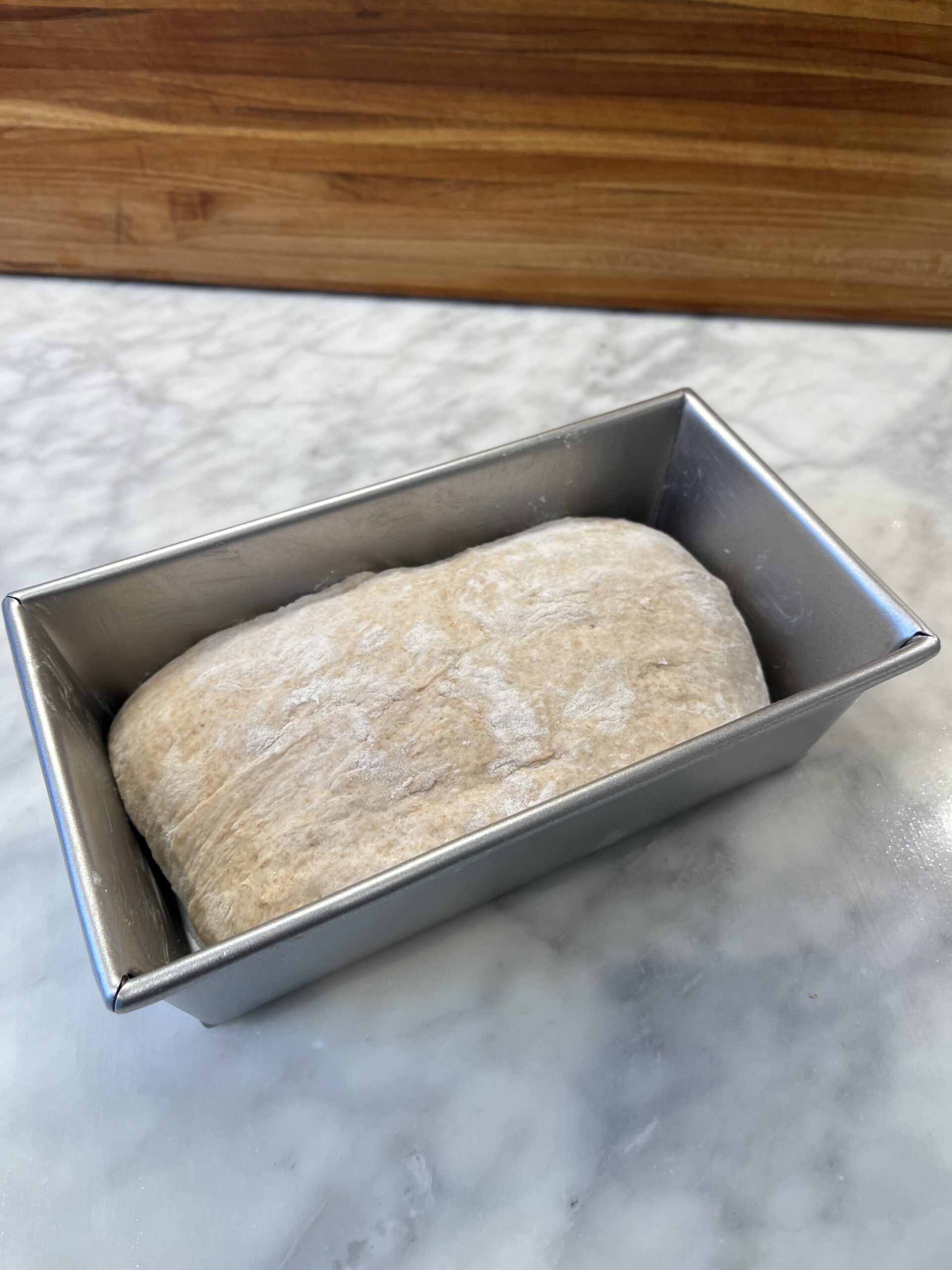 Photo of whole wheat sourdough sandwich dough, shaped in a metal pan before proofing.