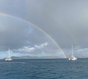 Two sailboats in Caribbean waters, a double rainbow and islands in the distance.