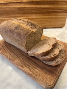 Loaf of whole wheat sourdough sandwich bread on a wooden cutting board with three slices.