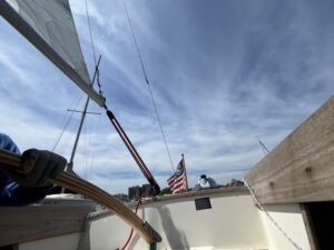 Photo on a Person Ensign sailboat looking aft showing a hand on the rudder and an American nautical ensign.