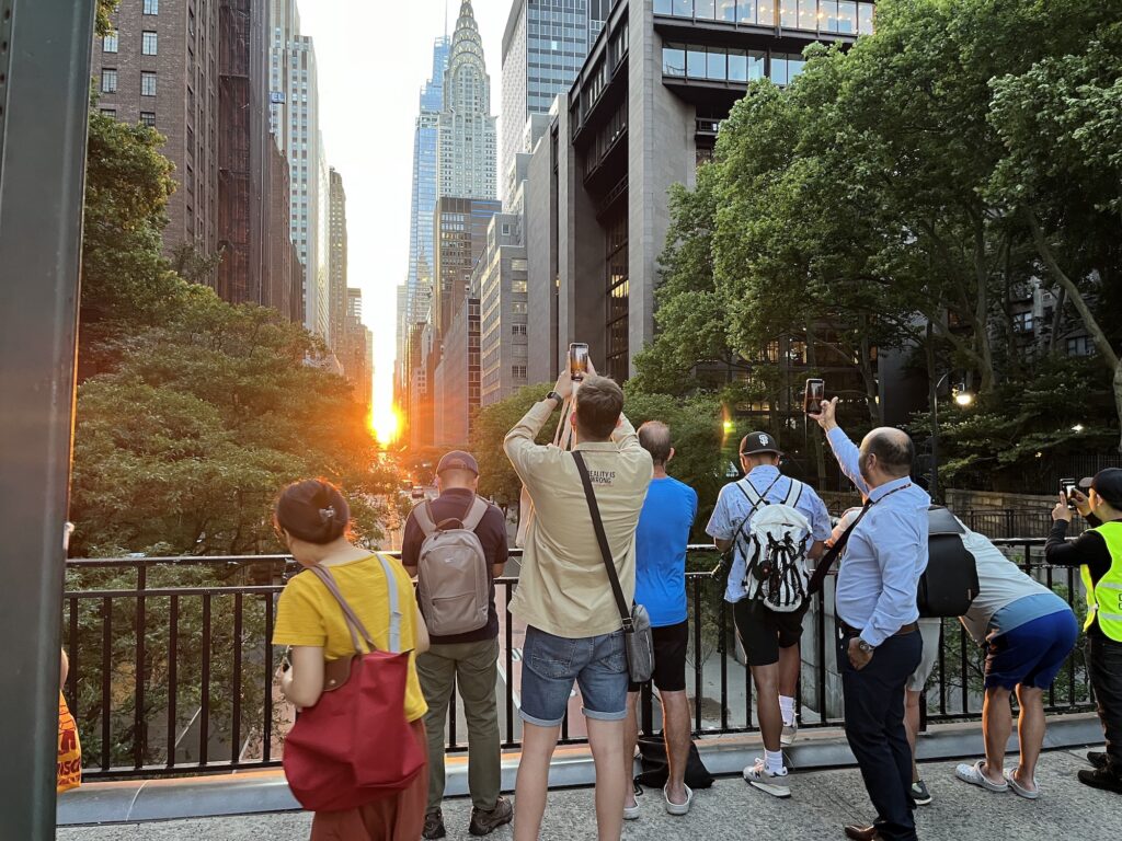 A group of people take pictures of a Manhattanhenge sunset on the Tudor City overpass.